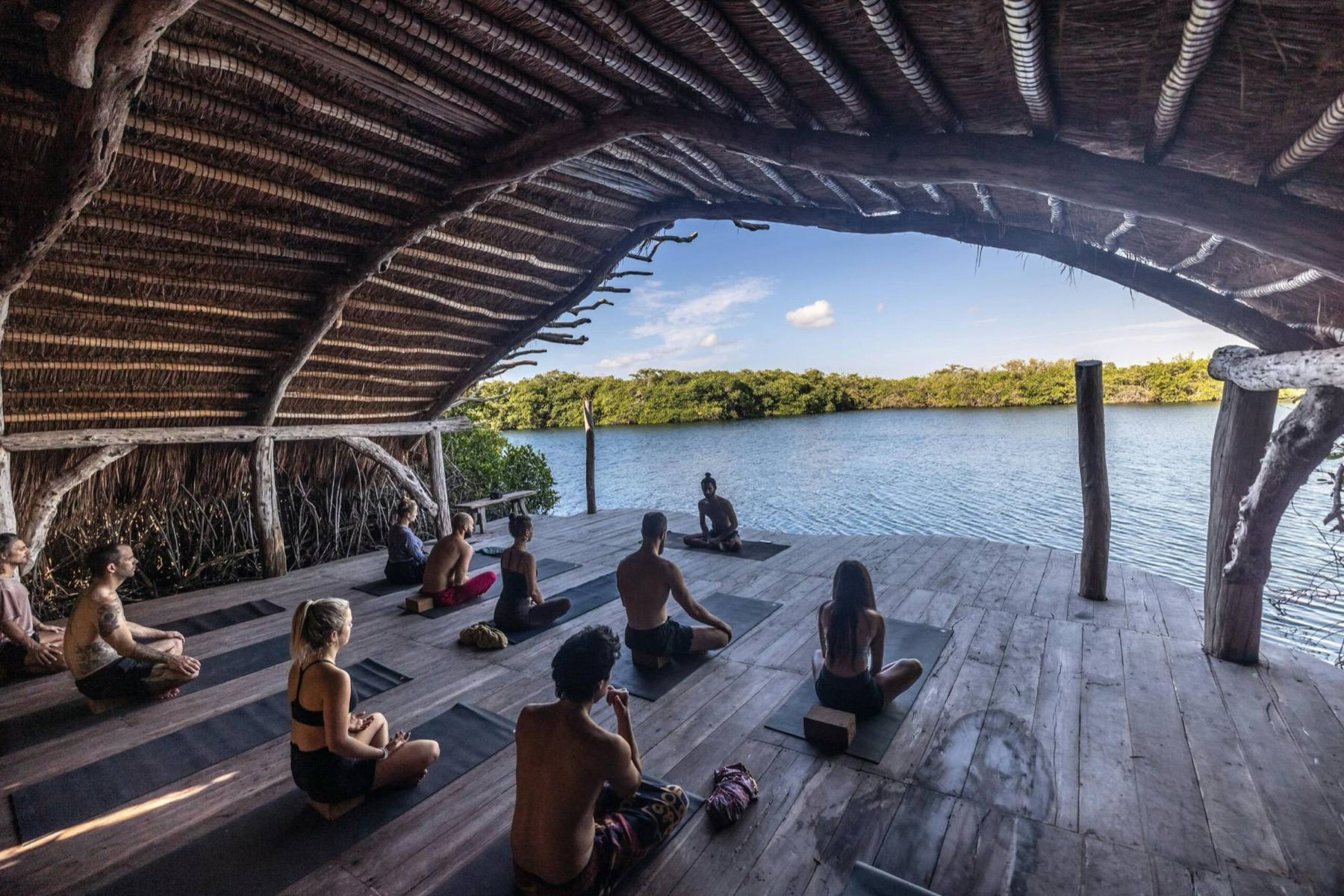 Meditación grupal guiada en una terraza de madera junto al agua